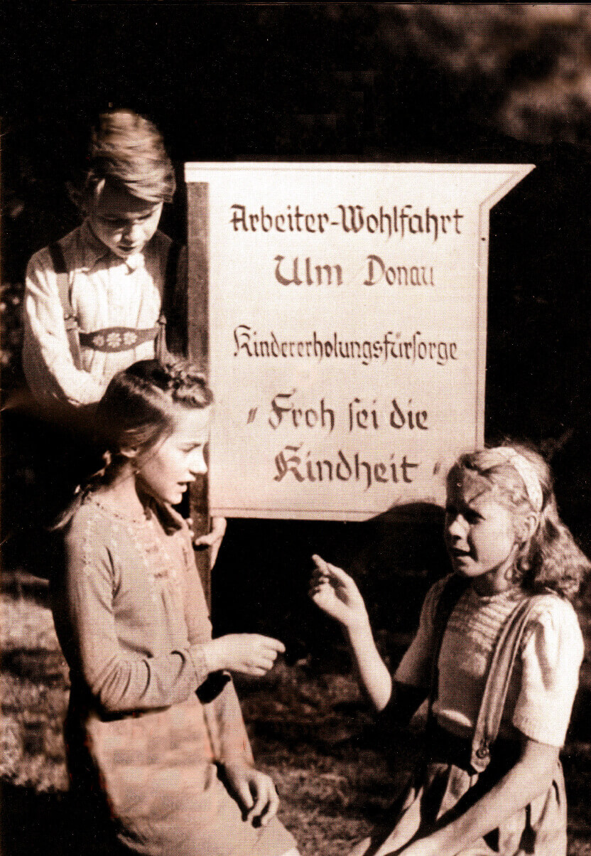 Kinder sitzen vor einem Schild der AWO